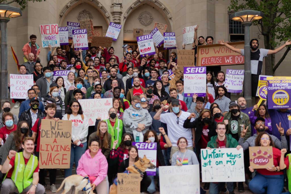 A large group of graduate workers at a rally, holding a variety of signs