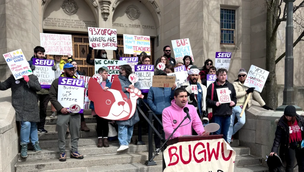 A photo of the BUGWU rally. People are gathered on the steps of Marsh Chapel carrying SEIU and BUGWU signs while one person speaks at the podium in front of the steps.